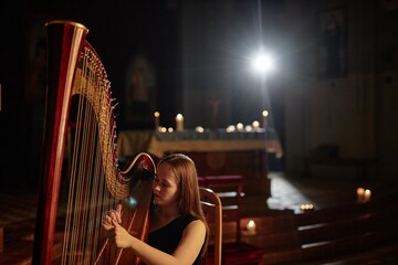 Chest up shot of young elegant woman playing harp softly giving classical music performance in...