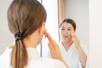 Young woman applying brown cushion on face with pad close-up front view.