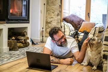 A man and his dog share a tender moment of communication, with the dog listening as the man speaks. He relaxes at home, using his laptop to browse the web, while the fire creates a cozy atmosphere