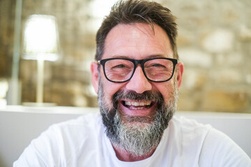 Mature man with glasses and a beard smiling confidently at the camera, in an indoor setting with a...