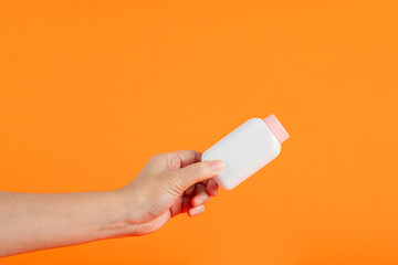 Baby talcum powder container in hand on orange background