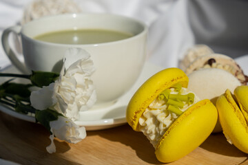 Sweet yellow macaron dessert Cup of green plant based matcha tea latte in cozy morning bed atmosphere. Creative holiday romantic date idea. Herbal prebiotic fiber superfood beverage antioxidant-rich