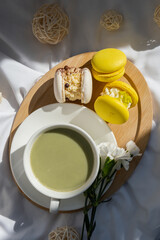 Nutrient-rich matcha drink with trendy macaron dessert on wooden tray in bed with fresh flowers. Morning beautiful breakfast present gift idea. Vibrant creative colors. Natural energy givers tea
