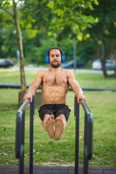 Young man wearing headphones doing dips on parallel bars in a park