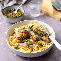Spaghetti pasta with meatballs in cream sauce on a plate on a background of stone or concrete.