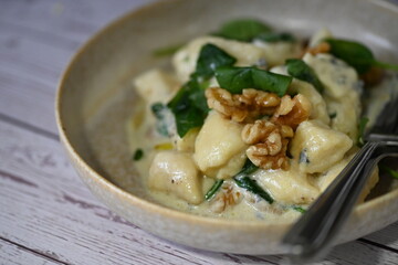 Close-up view of potato gnocchi served with a creamy blue cheese sauce and walnuts on a white plate. A rich and flavorful dish combining soft, pillowy gnocchi with the bold taste of blue cheese 