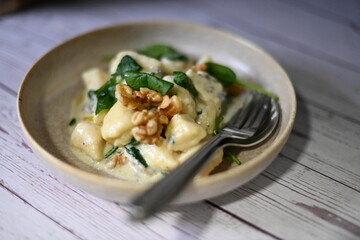 Close-up view of potato gnocchi served with a creamy blue cheese sauce and walnuts on a white plate. A rich and flavorful dish combining soft, pillowy gnocchi with the bold taste of blue cheese 