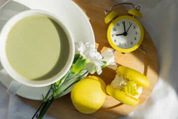 Yellow alarm clock time wake up Sweet yellow macaron dessert Cup of green plant based matcha tea latte in cozy morning bed atmosphere. Creative holiday romantic date idea. Herbal prebiotic fiber