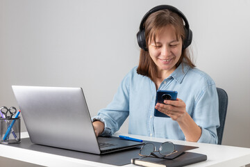 Young happy freelancer, smiling pretty professional businesswoman worker looking at smartphone, using cellphone mobile technology working at home or in office checking cell phone sitting at desk