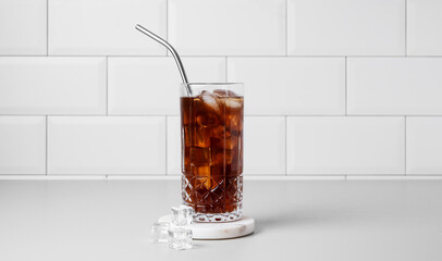 Cold brew coffee in a glass with ice and straw on a light table against a white brick background.