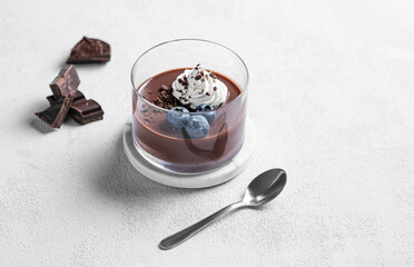 Chocolate pudding in a glass with whipped cream and fresh blueberry on a light background