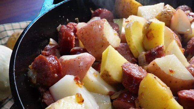 Cooking a dinner made with potatoes, kielbasa, spinach, onions and a mustard sauce.  Making dinner in the kitchen in a cast iron skillet.