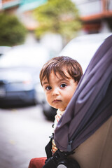 Portrait of a little boy peeking out of the baby carriage where he is sitting with an expression of curiosity