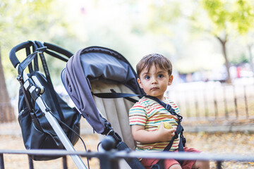 Little boy riding on a stroller in a park looks with curious expression