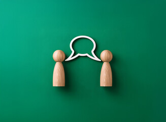 Two wooden figures face each other, a white speech bubble floats between them against a green background.  This symbolizes communication and dialogue.