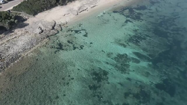 Drone footage of Rena di Levante on Capo Testa, Sardinia, Italy, in summer, showcasing golden sand, turquoise waters, rolling dunes, and stunning Mediterranean coastal scenery under clear skies.