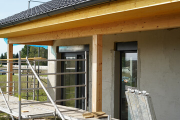 An outdoor environment of an unfinished new building. We see part of the unfinished house and scaffolding.