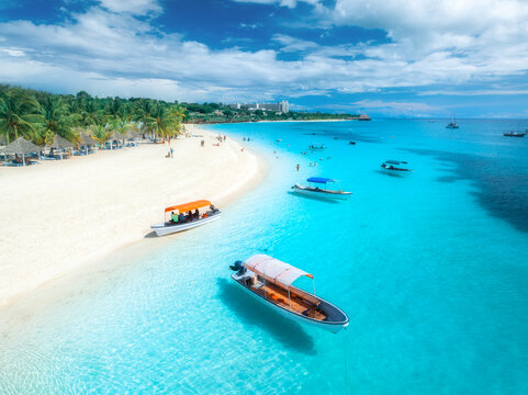 Aerial view of the boats on tropical sea coast with white sandy beach on summer sunny day. Vacation in Kendwa, Zanzibar. Landscape with boat, yacht, clear water, green palms, blue sky. Top drone view
