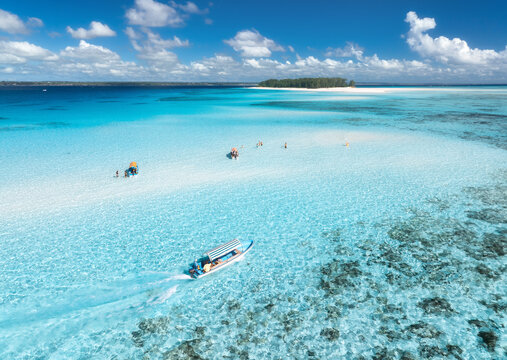 Aerial view of floating boat in transparent azure water on sunny summer day. Mnemba island, Zanzibar. Top view of yacht, sandbank in low tide, clear blue sea, sand, sky with clouds. Motorboat in ocean