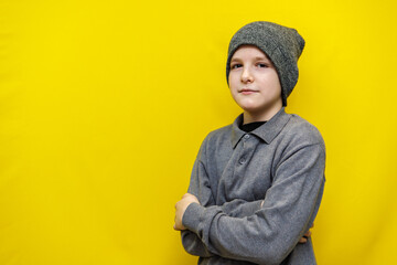 ten year old boy in grey knitted hat and sweater standing with arms folded on chest on yellow background
