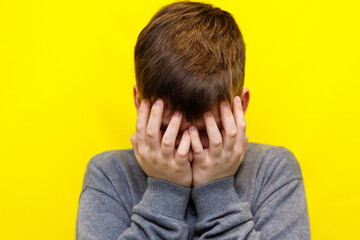 Fototapeta premium boy crying covering his face with both hands on yellow background