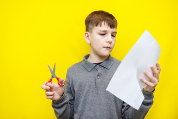 boy in grey sweater cuts out figure from white sheet of paper on yellow background