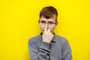 ten year old boy in grey sweater adjusts glasses on nose with index finger and looks at camera on yellow background