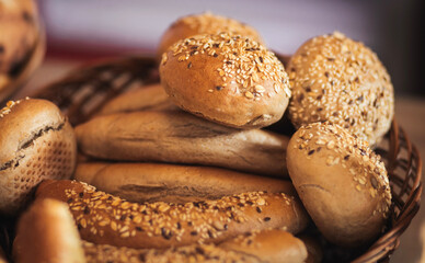 A basket filled with freshly baked bread rolls and baguettes topped with sesame and flax seeds, showcasing a golden crust and rustic charm. Perfect for bakery or culinary themes.