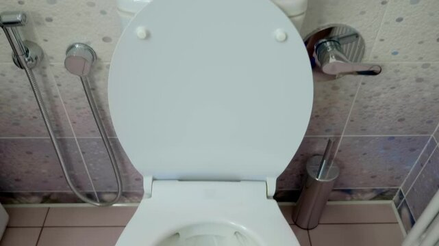 In the toilet, a man's hand presses the flush button on the toilet cistern, a strong stream of water flushes everything down the drain. Shot in motion