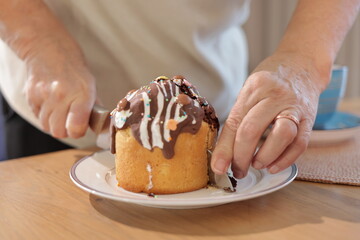 An Easter cake with white icing, colorful sprinkles, and a burning candle is arranged with red eggs, while a person adjusts items in the background.