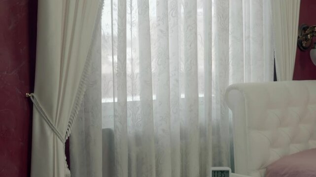 Bedroom window with beautiful white tulle and curtains hanging on a golden cornice and a white glossy stretch ceiling. Shot in motion