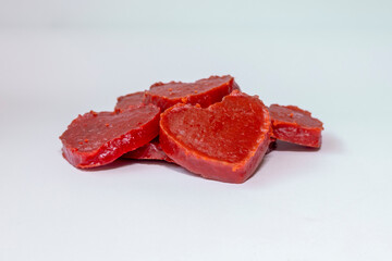 Heart shaped pumpkin candy with a shiny texture and intense red color, arranged on a light surface.