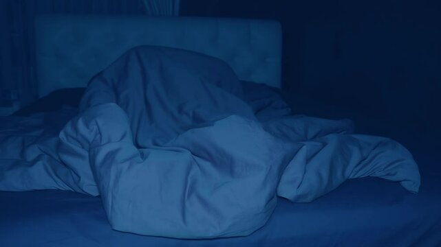 In the darkness of the bedroom bed, a man sleeps restlessly, constantly tossing and turning, his feet sticking out from under the blanket. Shot in motion