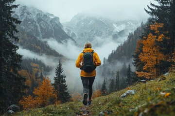 Obraz premium Early in the morning, a senior woman exercises by jogging in a foggy meadow with mountains in the backdrop
