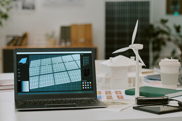Workspace featuring laptop displaying solar panel design, alongside wind turbine model. Emphasizing...