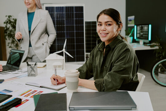 Hispanic woman smiling while working on sustainable project demonstrating renewable energy models in modern office environment engaged in team collaboration