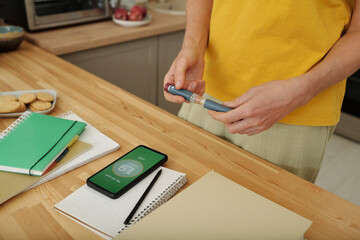 Closeup of woman with diabetes monitoring glucose levels with smartphone and holding injector pen copy space
