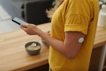 Close up shot of adult woman with diabetes using smartphone while making healthy breakfast in...