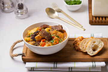 Delicious beef stew with vegetables in a white bowl on white background