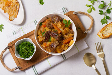 Delicious beef stew with vegetables in a white bowl on white background. High angle view