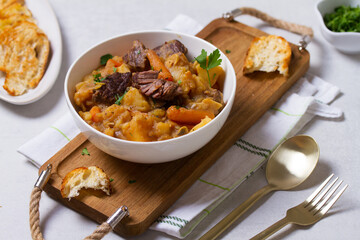Delicious beef stew with vegetables in a white bowl on white background