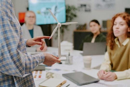 Close-up view of person holding wind turbine model while presenting sustainable energy to diverse group in office environment during meeting session