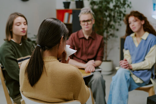Group therapy session involving four women sitting in a circle engaging in conversation. Shelves with books and plants in background, creating a cozy atmosphere