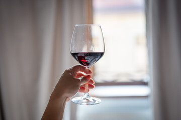 Female hand holding a glass of red wine in front of the window