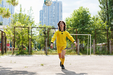 A young footballer in a yellow uniform juggles the ball on an outdoor playground, improving his control.