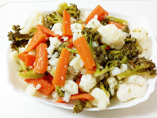 Mixed Organic Steamed Vegetables (Carrots, Broccoli and Cauliflower) on a Plate on a white wooden background, top view. Flat lay, overhead, from above.
