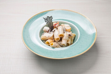 Tortiglioni pasta with carbonara-style sauce, crispy bacon bits, black truffle shavings, elegantly plated on light blue ceramic surface