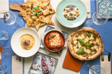 Delicious italian food, including pasta, pizza, lasagna, focaccia, and dessert, served on a table with wine glasses