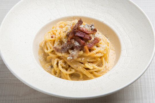 Creamy carbonara pasta with crispy guanciale and grated pecorino romano cheese, served in a stylish white plate
