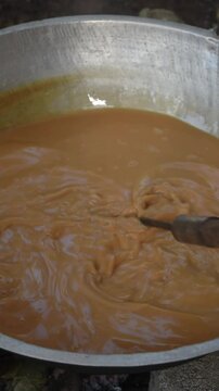 traditional method of making dodol in a large container, kaludodol in sri lanka, dark sweet candy, made from coconut milk, jaggery and rice flour, sticky thick sweet toffee, slow motion in 60fps